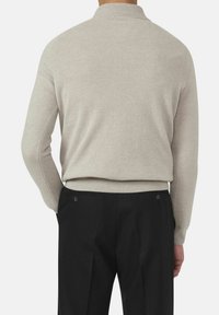 Beige gebreide trui met een geribbelde kraag, een zachte textuur en een aansluitend ontwerp, gecombineerd met zwarte op maat gemaakte broeken met knopen aan de achterkant.