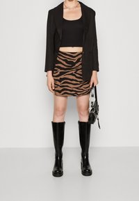 Blazer noir porté sur un haut court noir, associé à une mini-jupe marron avec un motif zébré noir, et des bottes noires montantes jusqu'aux genoux.