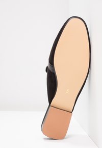 Semelle en daim noir avec un bord arrondi, dotée d'un talon en caoutchouc beige lisse et de rainures subtiles pour une meilleure adhérence. Taille marquée "5".