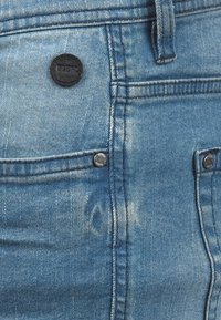 Blue denim jeans featuring a button with a black accent, light distressing, and classic five-pocket design.