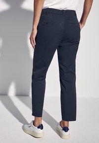 Marina byxor med rak benpassform, med en slät yta, elastisk midja och två bakfickor, tillsammans med vita sneakers.