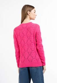 Maglione fucsia con texture a forma di diamante e piccoli motivi in rilievo. Maniche con bordo a coste e orlo. Indossato con jeans a vita alta.