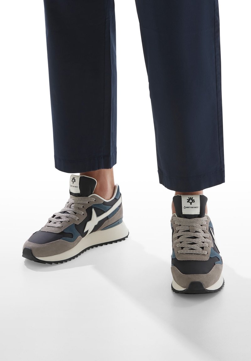 Sneakers sportivi con una combinazione di grigio, blu navy e bianco, caratterizzati da un design in suede e rete, colletto imbottito e suola in gomma testurizzata.