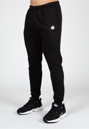 Zwarte sweatpants met een elastische tailleband, met een klein wit gorilla-logo op de dij. Gecombineerd met zwarte sport sneakers.
