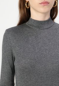 Grå turtleneck genser laget av et mykt, ribbet strikket stoff. Tett passform med lange ermer og minimale sømmer.