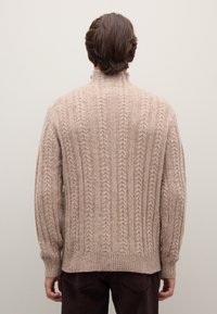 Maglione beige lavorato a maglia con colletto alto, caratterizzato da una texture a coste e un motivo a treccia, maniche lunghe e orlo dritto.