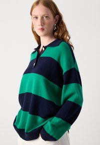 Grüner und navy gestreifter Pullover mit Kragen, der über drei Knöpfe, gerippte Bündchen und eine weiche Strickstruktur verfügt.