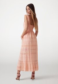 Maxi dress in light peach fabric with eyelet pattern, fitted bodice, and flared skirt. Features wide shoulder straps and scalloped hem.