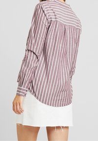 Chemise à manches longues à boutons, rayée bordeaux et blanche, confectionnée dans un tissu léger avec un ourlet arrondi et des poignets boutonnés.