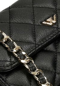 Sac en cuir noir matelassé avec une bandoulière chaîne dorée et un accent logo, mettant en valeur les détails texturés et un design élégant.