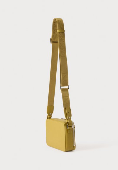 Small rectangular mustard-yellow crossbody bag with wide adjustable strap featuring embossed text and a top zipper closure.