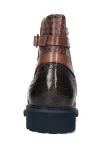 Botín de cuero marrón y negro con patrón texturizado, correa con hebilla y suela de goma negra, visto desde atrás sobre un fondo blanco.