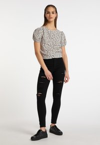 Bluse med pufærmer og blomstermotiv i creme, parret med høj talje sorte skinny jeans med slidte detaljer og sorte sneakers.