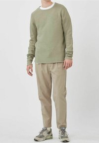 Vaaleanvihreä, teksturoitu pyöreäkauluksinen neule, kerrostettuna valkoisen aluspaidan päälle. Beigejä, kapealahkeisia housuja ja harmaat lenkkitossut, joissa on yksityiskohtia, täydentävät asun.