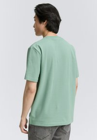 Camiseta de manga corta verde menta con un ajuste relajado, cuello redondo y textura de algodón suave, mostrada desde una vista trasera.