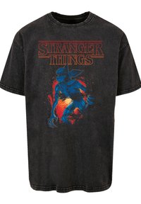 Black cotton t-shirt featuring a blue creature graphic with a red background, and "Stranger Things" text in orange at the top.