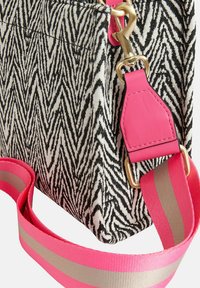 Černo-bílá taška z tkaniny se vzorem cikcak, zlatými kovovými doplňky a odnímatelným růžovým popruhem se šedými pruhy.