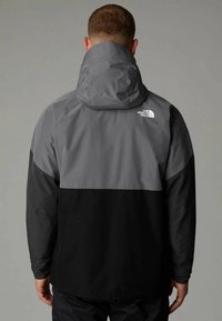 Veste pour homme en gris et noir, dotée d'une capuche, d'une texture lisse et d'un accent de logo dans le dos. Le design bicolore ajoute du contraste.