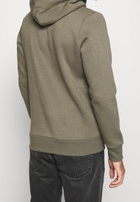 Ciemnooliwkowa bluza z kapturem z kieszenią kangurka, ściągaczami przy mankietach i u dołu. Miękki materiał o luźnym kroju i kapturem. Gładki, prosty wzór.