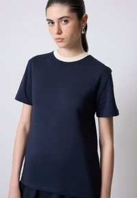 Mørkeblå t-shirt med en cremefarvet ribbet halsudskæring. Korte ærmer og en afslappet pasform, lavet af et glat, let stof.