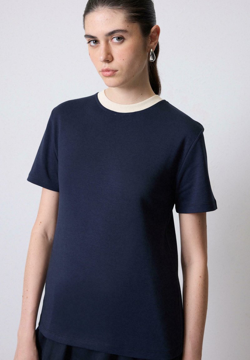 Mørkeblå t-shirt med en cremefarvet ribbet halsudskæring. Korte ærmer og en afslappet pasform, lavet af et glat, let stof.