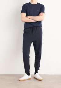 Marinblå bomullströja med rund halsringning och liten logotyp, tillsammans med mörka joggingbyxor med dragsko och ribbade mudd, bärs med vita sneakers.