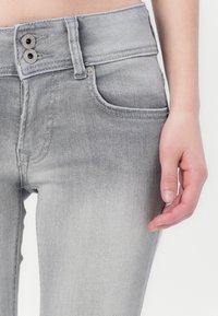 Grå denimjeans med en to-knapps lukking, frontlommer og en jevn tekstur. Har subtile falminger rundt lårene.