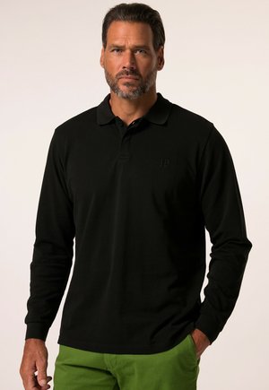 Czarna longsleeve polo z kołnierzykiem, z subtelnym logo i ściągaczami na rękawach, w połączeniu z zielonymi spodniami. Gładka faktura materiału.