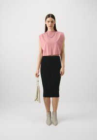 Rózsaszín cropped, ujj nélküli top, bordázott fekete ceruzaszoknya, bézs bokacsizma és semleges színű kézitáska. Simogató textúrák és testhezálló dizájn.