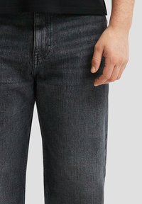 Jeans in denim scuro con vestibilità slim, caratterizzati da una leggera sbiaditura, design a cinque tasche e chiusura con zip. La texture appare liscia e robusta.
