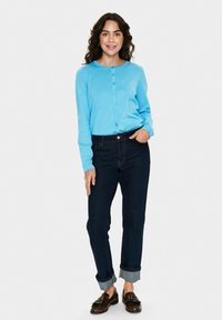 Vaaleansininen pitkähihaisen nappipaidan yhdistelmä tummien farkkujen ja ruskeiden loafer-kenkien kanssa. Paidassa on pyöreä kaula-aukko ja teksturoitu kangas.