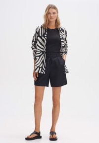 Chemise légère à rayures noires et blanches, haut noir, shorts sombres ajustés et sandales noires à semelle épaisse. Design simple, coupe décontractée.