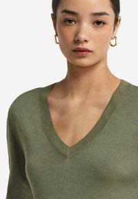 Oliwkowy sweter dzianinowy z dekoltem w kształcie V i prążkowanym wykończeniem, o gładkiej fakturze i dopasowanym kroju.