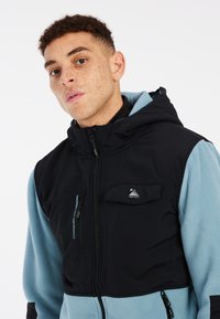 Zwarte en blauwe hoodie met rits aan de voorkant, voorzien van een ritszak en een zachte textuur, ontworpen voor actieve kleding.