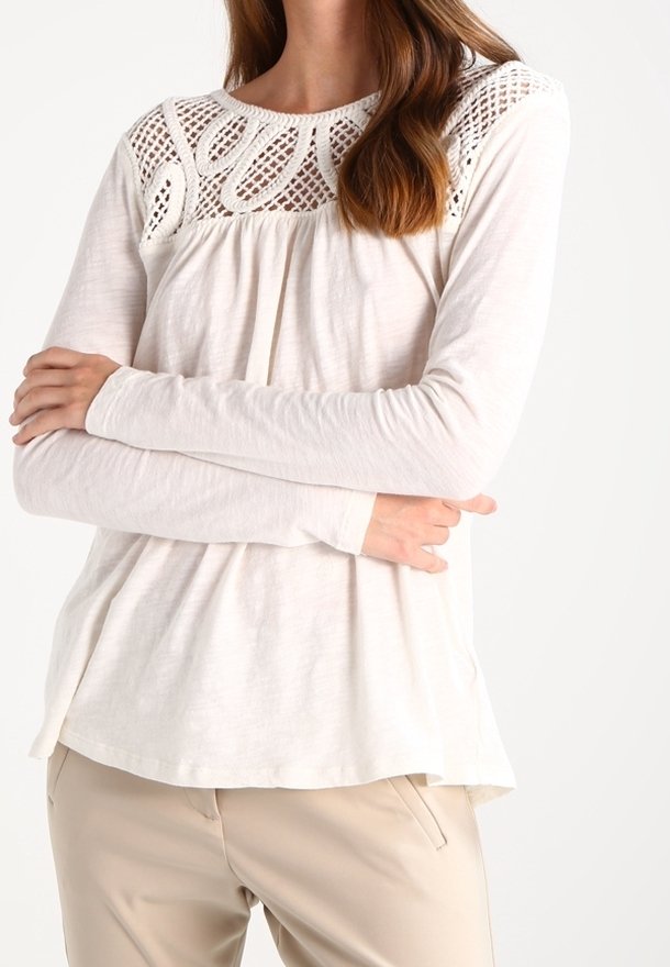 Långärmad topp i krämfärg med en texturerad virkning på axlarna, med en avslappnad passform och mjukt tyg. Rundad nederkant med mjuka draperingar.