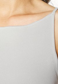 Top de alças canelado cinza claro, com uma leve elasticidade, decote amplo e alças finas; o tecido texturizado realça o interesse visual.