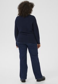 Navy ribbed sweater with a rounded hem, paired with dark blue wide-leg jeans and black shoes, viewed from the back. Curly hair visible.