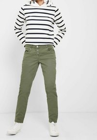 Sweat à capuche rayé blanc et marine, avec une capuche. Pantalon vert olive avec braguette à boutons et poches avant. Porté avec des baskets montantes blanches.