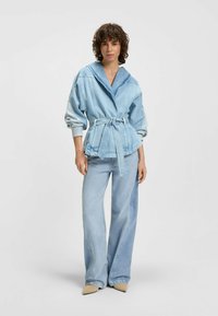 Jasnoniebieska kurtka dżinsowa z szerokim kołnierzem, talią podkreśloną paskiem, zestawiona z pasującymi jasnoniebieskimi spodniami dzwonami.