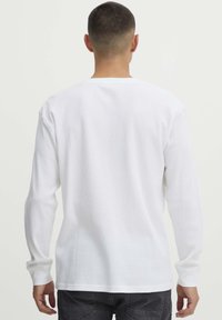 Witte thermoshirt met lange mouwen, ribbelstructuur, ronde hals en omgeslagen mouwen. Eenvoudig ontwerp zonder zichtbare patronen of accenten.