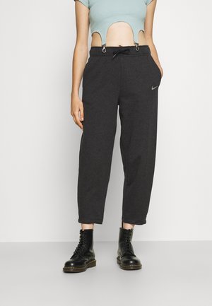 Persoon draagt donkergrijze Nike joggingbroek met koordsluiting in de taille en zwarte veterlaarzen, korte lichtblauwe top met uitsnijdetails.