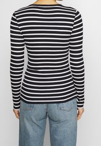 Maglia a maniche lunghe a righe bianche e nere con scollatura rotonda, realizzata in tessuto a costine. Indossata con pantaloni di jeans blu chiaro.