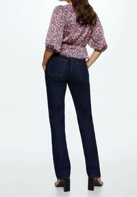 Jeans in denim scuro con taglio dritto, caratterizzati da cuciture visibili e due tasche posteriori, abbinati a un top a maniche puff con motivo floreale.