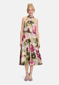 Robe midi sans manches à fleurs avec une taille froncée, présentant de grandes fleurs roses, vertes et jaunes sur un fond clair ; avec un col halter noué.