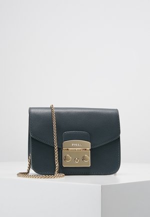 Sort læder Furla crossbody taske med guldkæde-rem og guldlås, placeret på en hvid overflade mod en ensfarvet baggrund.