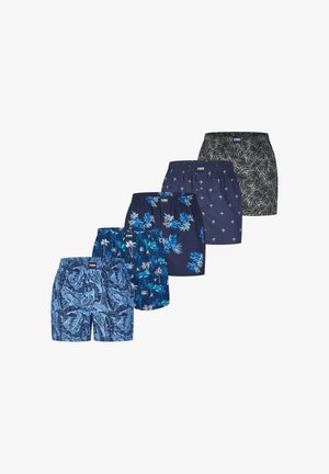 Cinque paia di pantaloncini da nuoto da uomo con fantasie tropicali e di foglie di palma in blu e nero, disposti affiancati in fila.