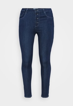 Temno modri traper skinny jeans z visokim pasom, ki imajo pet gumbov spredaj, standardno obliko žepov in gladko teksturo.