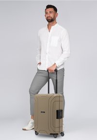Hartschalentrolley in khaki mit strukturierter Oberfläche, ausgestattet mit einem schwarzen Teleskopgriff und Doppelrollen für optimale Mobilität.