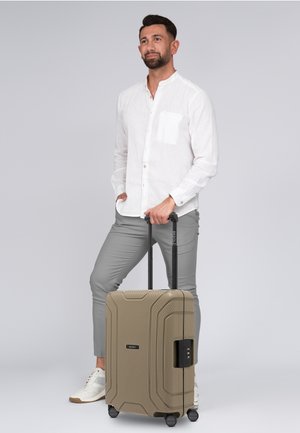 Harde koffer in khaki met een gestructureerd oppervlak, uitgerust met een zwarte telescopische handgreep en dubbele wielen voor wendbaarheid.
