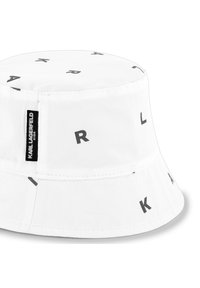 Chapeau seau blanc en coton, ornée de lettres noires imprimées "K", "A", "R" et "L" disposées de manière éparpillée. Étiquette logo noire sur le côté.
